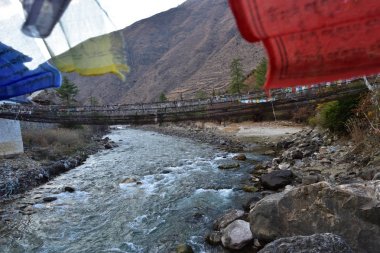 Butan renkli dua bayrakları ile nehir üzerinde yürüyen asma köprü