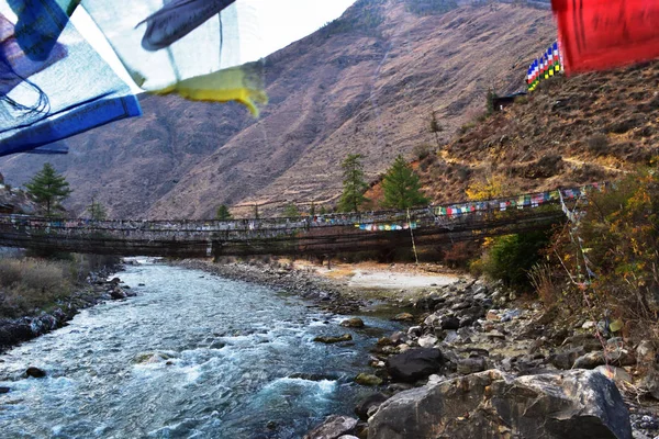 Pont suspendu de marche sur la rivière avec des drapeaux de prière colorés au Bhoutan — Photo