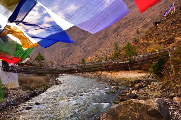 Pont suspendu de marche sur la rivière avec des drapeaux de prière colorés au Bhoutan — Photo