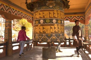 Bir Bhutanlı adam ve turistler bir Budist pagoda bir dua tekerleği döner .