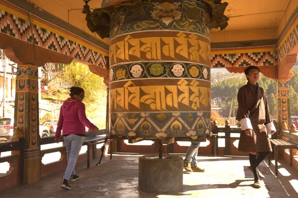 A Bhutanese man and tourists rotates a prayer wheel in a Buddhist pagoda . — Stock Photo, Image