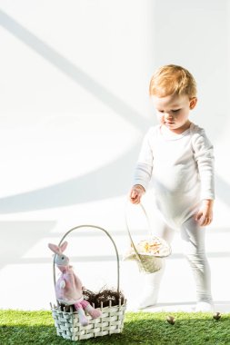 adorable baby standing near straw basket with decorative rabbit on white clipart