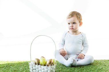 sevimli bebek beyaz üzerinde izole Doğu yumurta renkli saman sepeti yakın yeşil çim üzerinde oturan