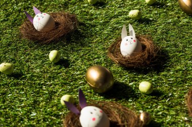 colorful Easter eggs, and chicken eggs with funny rabbit faces and paper ears on green grass   clipart