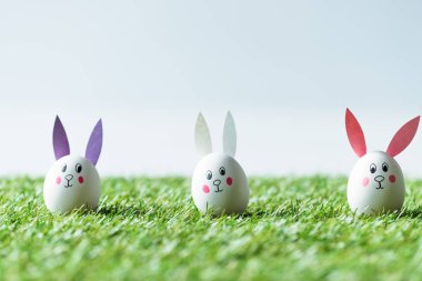 yeşil çim üzerinde komik tavşan yüzleri ve kağıt kulakları ile Doğu tavuk yumurtaları seçici odak 