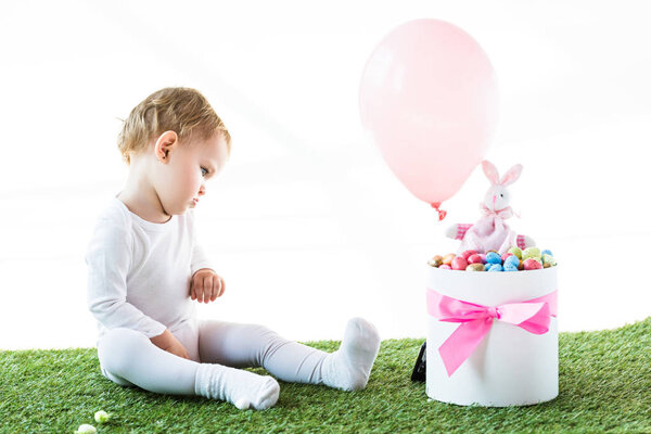 милый ребенок сидит рядом с коробкой с Estern яйца, декоративные кролика и воздушный шар изолированы на белом
