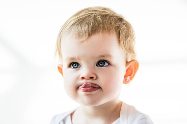 adorable child with blonde hair showing tongue isolated on white
