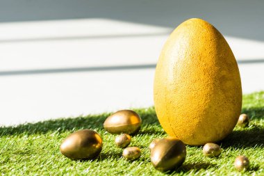 yeşil çim yüzeyinde sarı devekuşu yumurta ve altın Paskalya yumurtası