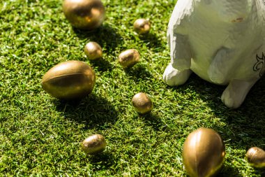 golden Easter eggs and decorative rabbit on green grass surface clipart