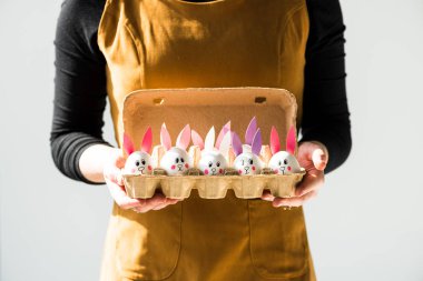 komik Bunny yüzler ve gri üzerinde izole kağıt kulakları ile tavuk yumurtası ile yumurta tepsisi tutan kadın kısmi görünümü