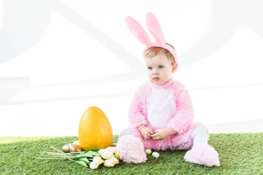 sarı devekuşu yumurta, renkli Paskalya yumurtaları ve beyaz üzerinde izole lale yakın oturan komik Bunny kostüm sevimli çocuk