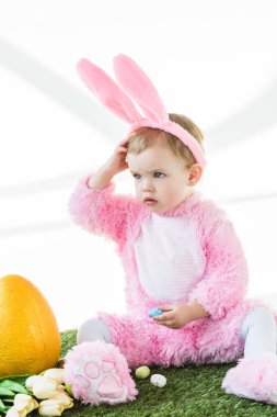 sarı devekuşu yumurta, renkli Paskalya yumurtaları ve beyaz üzerinde izole lale yakın oturan komik Bunny kostüm sevimli çocuk