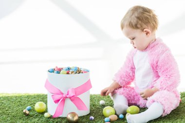pembe sevimli çocuk beyaz üzerinde izole renkli Paskalya yumurtası kutusu yakın yeşil çim üzerinde oturuyor