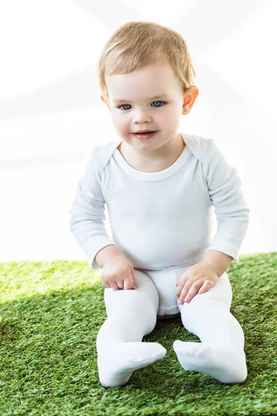 白に孤立した緑の草の上に座ってブロンドの髪を持つ愛らしい笑顔の赤ちゃん — ストック写真