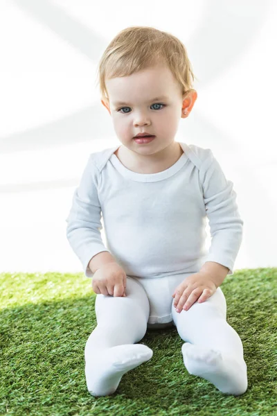 可爱的微笑的婴儿与金发坐在绿草孤立的白色 — 图库照片