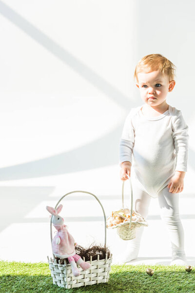 милый ребенок держит соломенную корзину, стоя на зеленой траве на солнце
