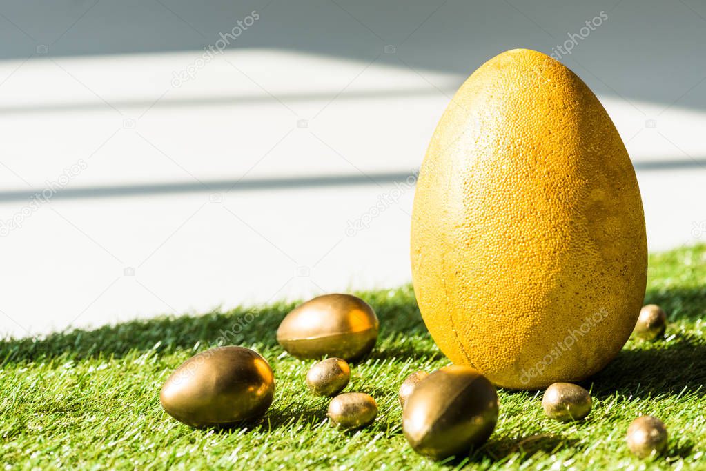yellow ostrich egg and golden Easter eggs on green grass surface