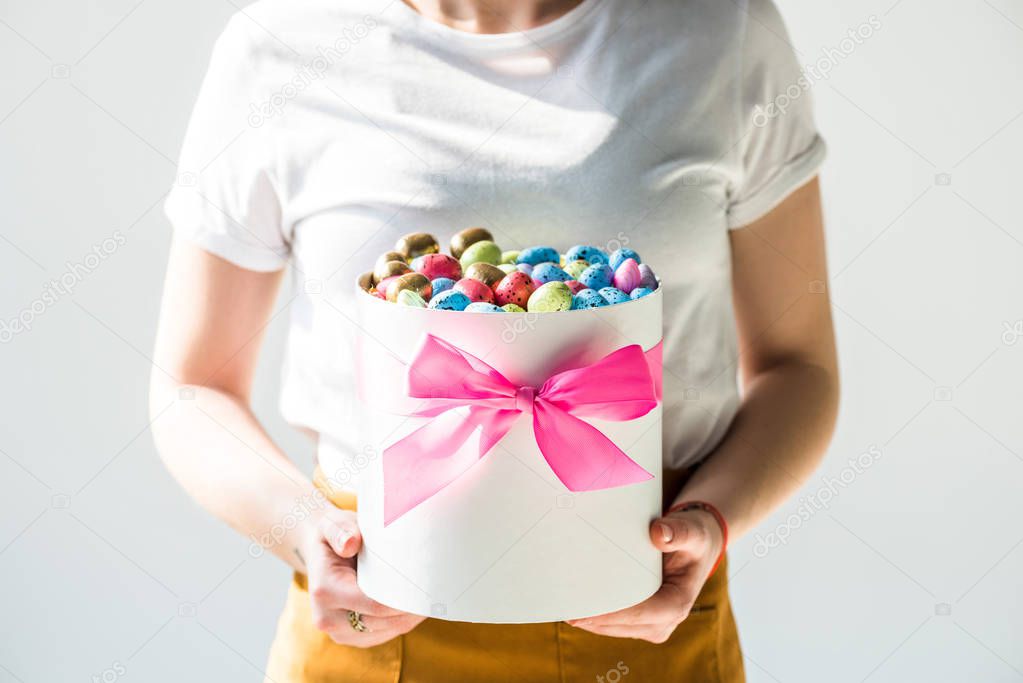 cropped view of woman holding round box full of colorful Easter eggs isolated on grey