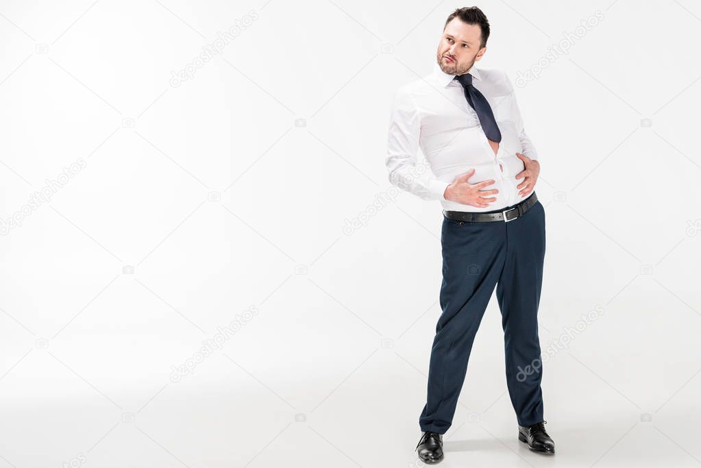 overweight man in tight formal wear touching belly and posing on white with copy space
