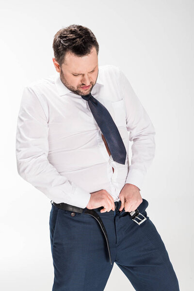 overweight man in formal wear putting on tight pants on white