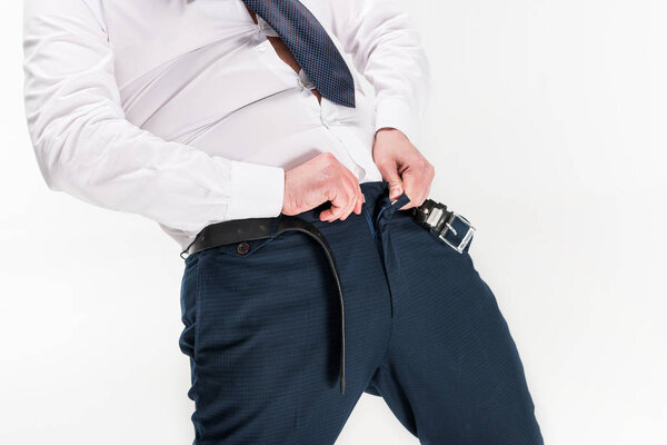 cropped view of overweight man in formal wear putting on tight pants isolated on white