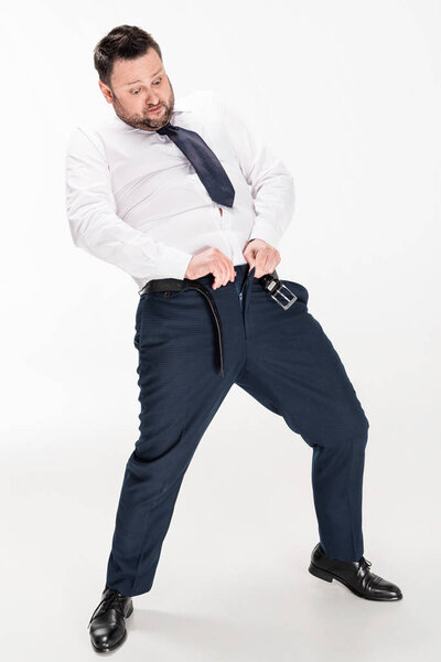 overweight man in formal wear putting on tight pants on white