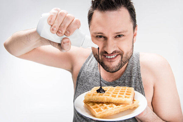 smiling chubby man pouring chocolate syrup on waffles on white
