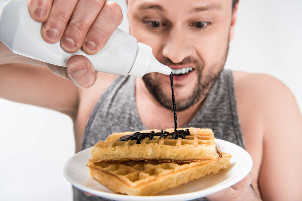 close up view of chubby man pouring chocolate syrup on waffles isolated on white