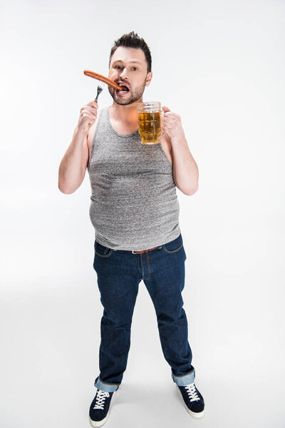 overweight man biting sausage and holding glass of beer on white