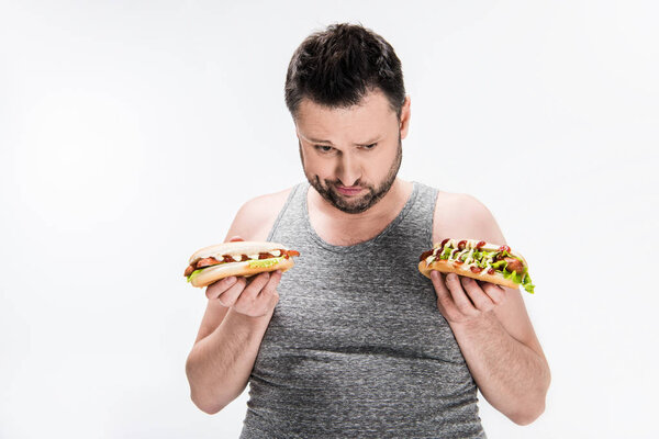 overweight man in tank top holding hot dogs isolated on white