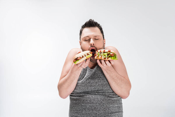 overweight man eating hot dogs isolated on white