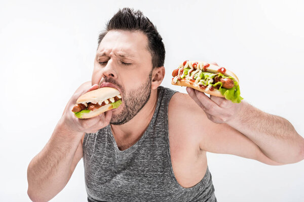 hungry overweight man in tank top eating hot dog isolated on white