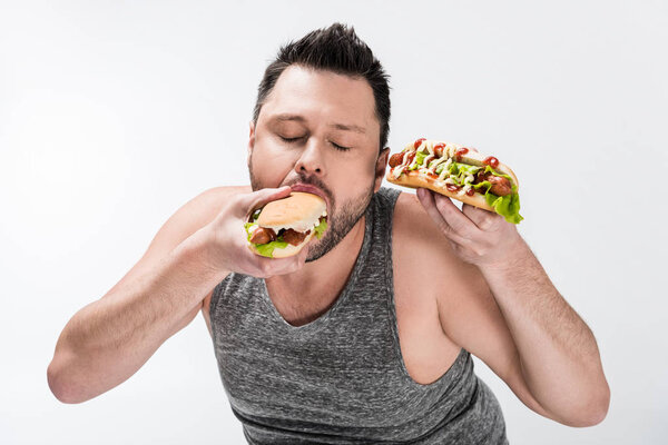 overweight man in tank top eating tasty hot dog isolated on white