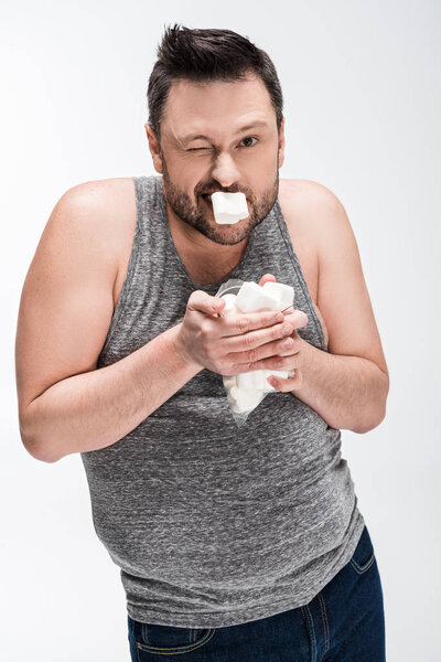 overweight man in grey tank top eating marshmallows isolated on white