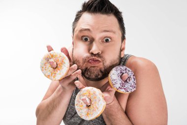 chubby man making face expression while holding donuts and looking at camera isolated on white clipart