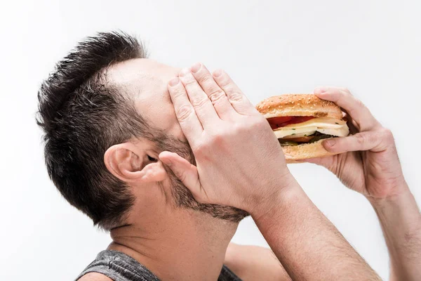 Pria Gemuk Berjanggut Menutupi Wajah Dengan Tangan Sementara Makan Burger — Stok Foto