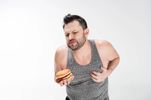 Hombre Con Sobrepeso Sosteniendo Hamburguesa Tocando Pecho Blanco Con Espacio — Foto de Stock