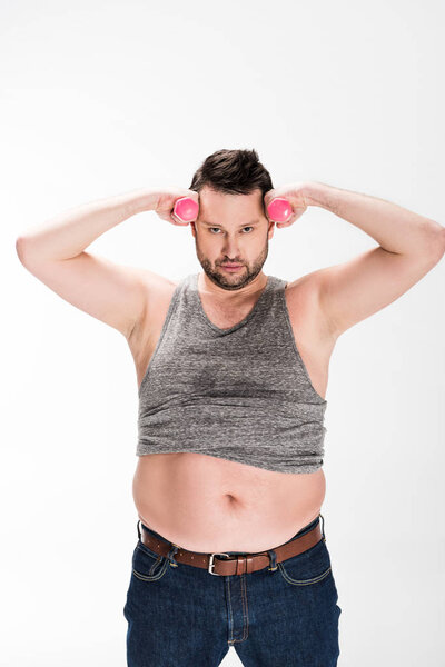 overweight man looking at camera while working out with pink dumbbells isolated on white