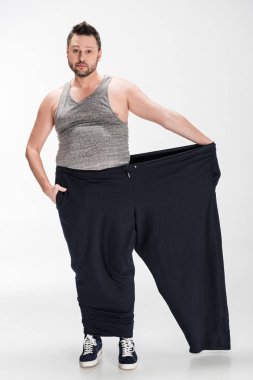 kilolu adam kilo kaybı ndan sonra büyük boy pantolon tutarak ve beyaz kamera bakarak