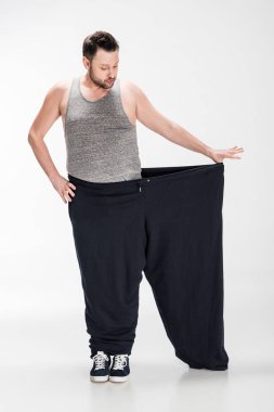 overweight man in tank top holding oversize pants after weight loss on white clipart