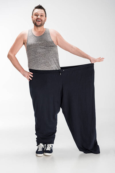 Мужчина с избыточным весом, держащий брюки большого размера после потери веса на белом
