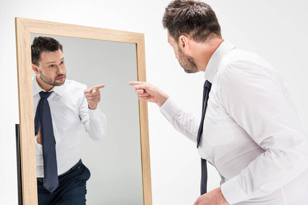 overweight man in formal wear pointing with finger at reflection in mirror on white