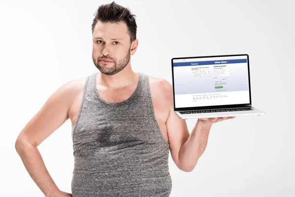 Übergewichtiger Mann Blickt Kamera Und Hält Laptop Mit Facebook Website — Stockfoto