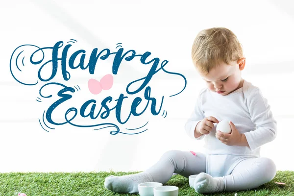 孩子坐在绿草地上用白鸡蛋靠近蓝色快乐复活节字母 — 图库照片