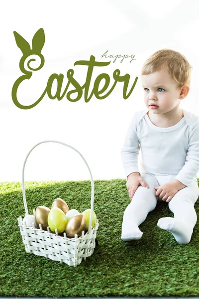 孩子坐在绿草旁 篮子附近有复活节彩蛋和上面的复活节快乐字母 — 图库照片
