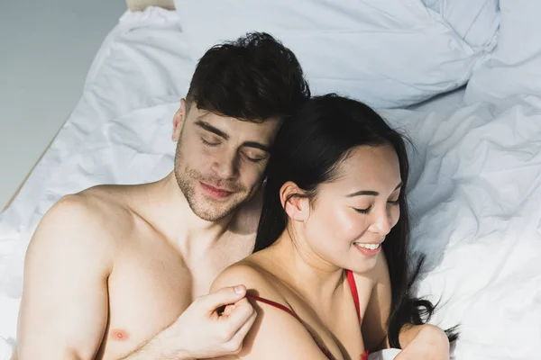 Young Smiling Multicultural Couple Lying White Bedding Sunshine — 스톡 사진