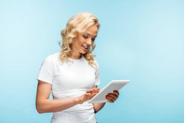 mavi üzerinde dururken dijital tablet kullanarak mutlu sarışın kadın 