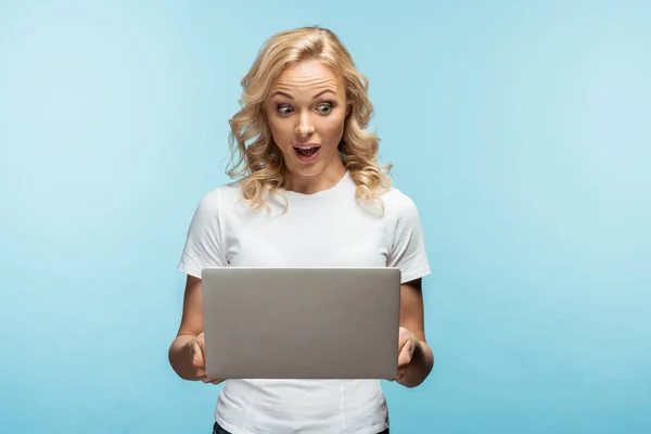 Geschokt Krullend Blonde Vrouw Kijken Naar Laptop Terwijl Staande Blauw — Stockfoto