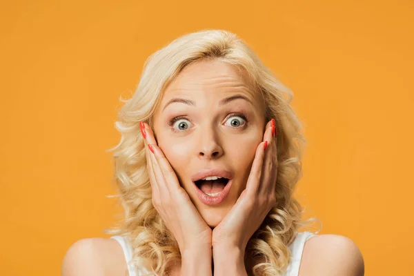 Geschokt Blonde Vrouw Kijken Naar Camera Aanraken Gezicht Geïsoleerd Oranje — Stockfoto