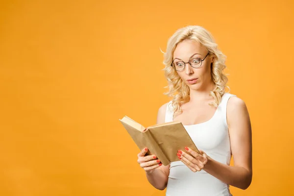 Έκπληκτος Ξανθιά Γυναίκα Γυαλιά Διαβάζοντας Βιβλίο Απομονωμένη Στο Πορτοκαλί — Φωτογραφία Αρχείου